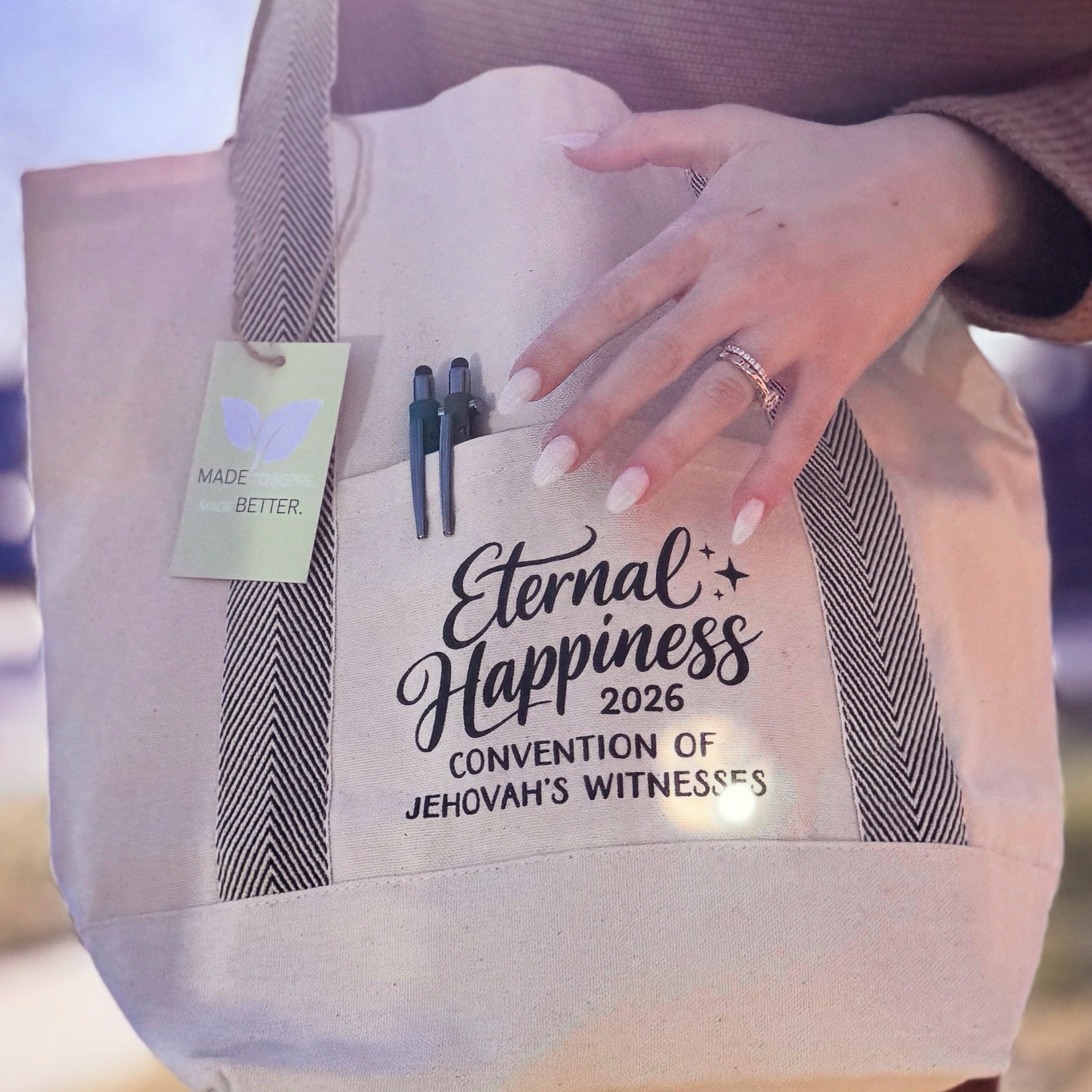 Person holding a tote bag with 'Eternal Happiness 2026 Convention of Jehovah's Witnesses' text.