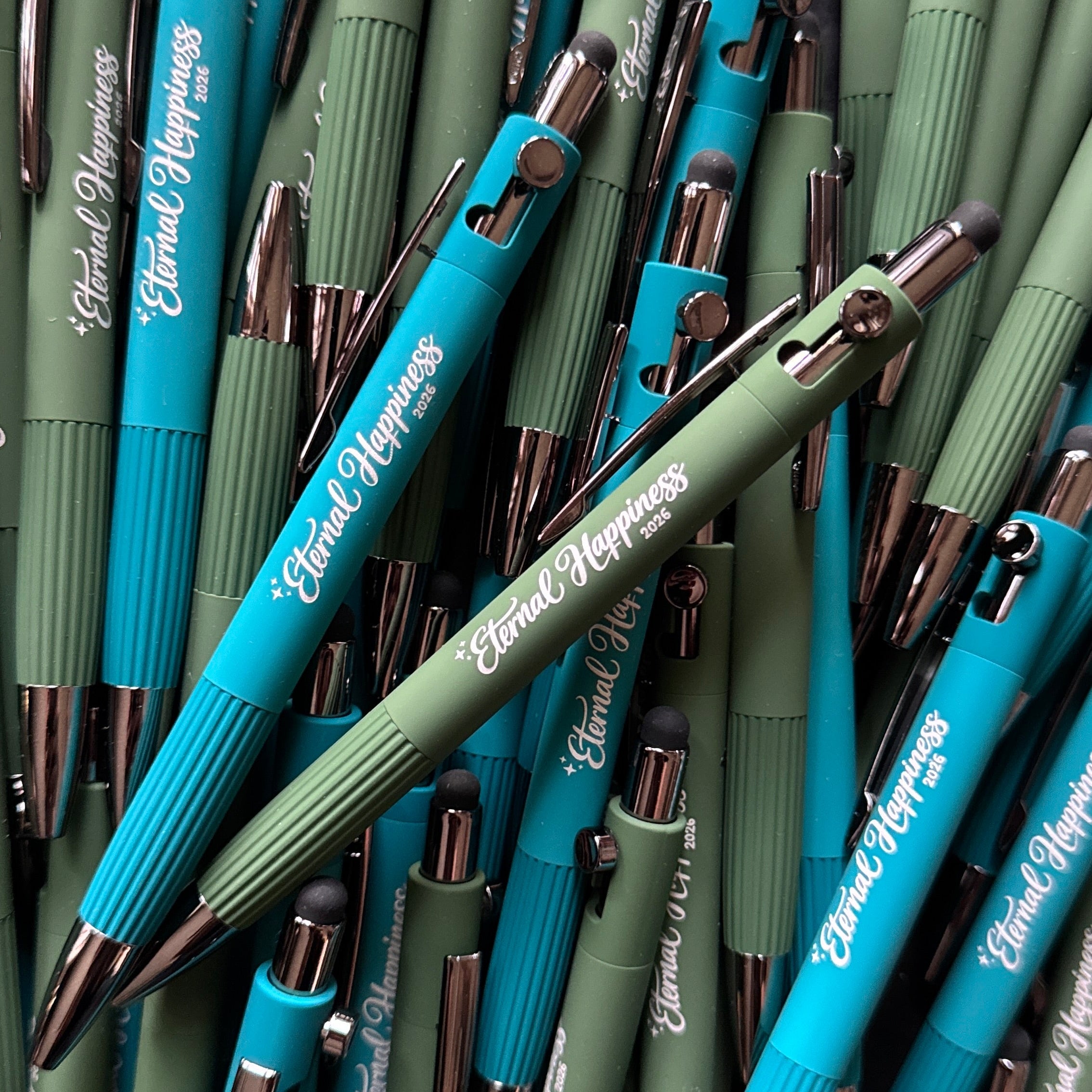 Collection of green and blue metal stylus pens with "Eternal Happiness 2026" engraving.
